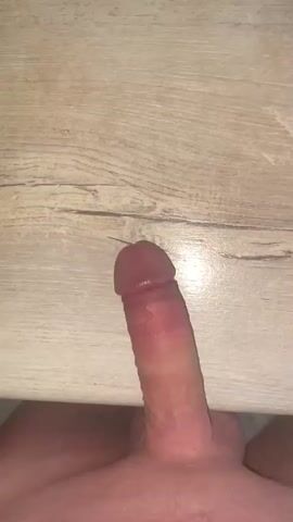 The video displays a close-up, low-angle shot of a penis resting against a light-colored wooden surface. The penis is partially exposed, with the glans visible and appearing slightly pink and moist. The texture of the wood grain is discernible in the background. The lighting suggests an indoor setting, possibly artificial light, as there are no strong indications of natural light sources like windows or sunlight. The focus is solely on the anatomical subject against the neutral backdrop. No text is visible in the media. The location context provided is "Нарынка, Russia," but there are no visual cues within the video that directly confirm or deny this location. The overall presentation is static, with no discernible activity or event taking place beyond the static display of the subject.