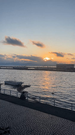 Person sits by moored boat during Fujisawa waterfront sunset