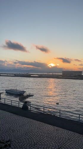 Person sits by moored boat during Fujisawa waterfront sunset