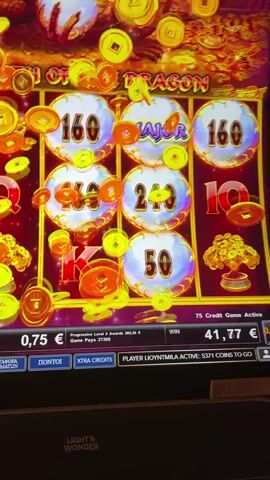 A close-up shot of a slot machine game screen displays the game "FORTUNE OF THE DRAGON". The reels are spinning with symbols including coins, a dragon, and card suits. The screen shows betting information, including a bet of 0.75 euros, a win amount of 70.27 euros, and other game statistics. Coins are animatedly falling onto the screen, indicating a win. The machine appears to be in operation.