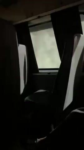 The video shows the interior of a bus at night. The seats are dark and gray, and the window is visible with dark curtains on either side. Outside the window, the sky is bright. A person wearing pants sits in one of the seats. The bus appears to be in motion.