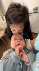 Young girl interacts with baby in grey outfit