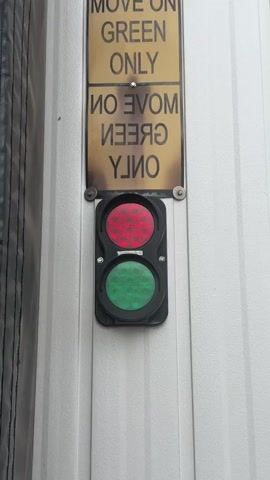 A close-up shot shows a red and green traffic light with a sign above it that reads "MOVE ON GREEN ONLY". The traffic light is mounted on a white ribbed surface. The red light is illuminated, and the sign above the light is slightly weathered and stained.