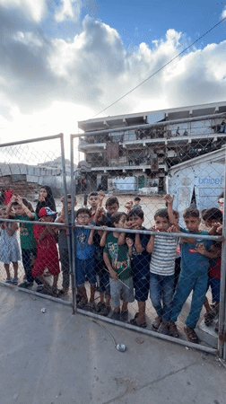Children peer through metal fence in Gaza