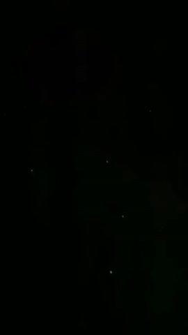 The video shows a dark sky with several small, white, pinprick-like lights scattered across it. Some of the lights are grouped together, while others are more isolated. The overall impression is of a starry night sky, possibly with a faint green or bluish haze in the background. The lights appear to be stationary.