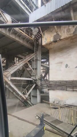 The video presents a low-angle view of complex metal structures and concrete walls, possibly within an industrial setting or an old, decaying building. The camera appears to be inside a vehicle or compartment, with a portion of the dashboard visible. The metal structures consist of beams, ladders, and walkways, showing signs of rust and age. Some parts are painted or covered with corrugated metal. The concrete walls are worn, with peeling paint and stains. The lighting is subdued, creating a somewhat ominous atmosphere.