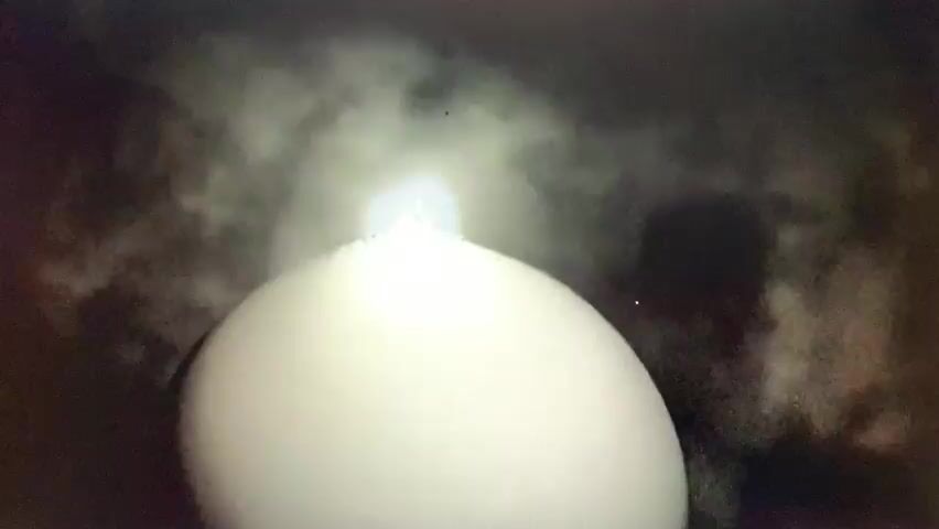 The media file depicts an abstract, computer-generated animation. The central subject is a large, spherical object that appears to be cracking and breaking apart. The surface of the sphere is covered in a tessellated pattern of lines, resembling a cracked eggshell or a fractured globe. As the animation progresses, pieces of the sphere are seen to fragment and fly outwards, disintegrating into smaller particles.

Above the breaking sphere, there is a bright light source, possibly representing a sun or a powerful explosion, emitting light and emanating wisps of smoke or cloud-like material. This light seems to be the catalyst for the sphere's disintegration. The background is dark and appears to be a night sky, with hints of smoke or atmospheric disturbances.

The overall mood is dramatic and possibly ominous, suggesting destruction, emergence, or transformation. There are no visible people or specific location cues within the animation itself. The setting is abstract and symbolic, focusing on the event of the sphere breaking apart and the light emanating from within. The time of day is not definitively discernible due to the abstract nature of the animation and the dark background, but the bright light suggests a powerful event occurring against a dark backdrop. No text is visible in the media file. Given the provided location context of Pisochyn, Ukraine, the animation might be interpreted as a symbolic representation of events occurring in that region, though this is speculative and not directly conveyed by the visual content alone.