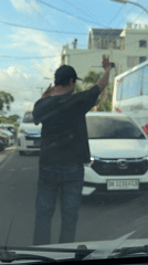 Person raises arm on Kuta street near tour bus
