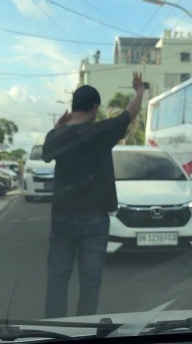 Person raises arm on Kuta street near tour bus