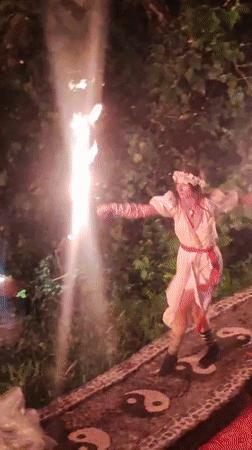 Fire dancer performs torch routine on decorated pathway in Blahbatuh
