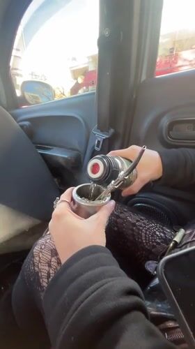 Person prepares traditional mate drink inside car in Buenos Aires