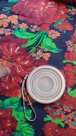 A hand is shown holding a white collapsible cup. The cup is initially flat, then it is turned around to reveal an image of a cartoon pig. The background is a fabric with a floral pattern.
