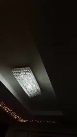 The video shows a rectangular crystal chandelier mounted in a recessed ceiling. The camera pans slightly to the right to show a decorative molding with floral patterns around the edge of the ceiling. The room appears to be dimly lit.