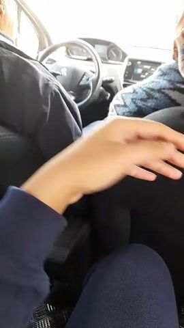 The video shows the view from the passenger seat of a car, with a person's hand moving in the foreground, as if keeping time with the music.  The car's interior is visible, including the steering wheel, dashboard, and seat coverings. A person is driving the car, and a passenger is in the front seat next to the videographer. The lighting suggests it is daytime.