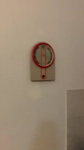 The video shows a panning view of a wall with shelves. On the left side of the wall, there is a vintage clock. The shelves contain various decorative items including vases, teapots, jars, and woven mats. The background is a plain white wall and a tiled section.