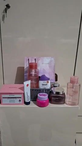 The video shows a collection of skincare products arranged on a shelf. The products vary in size, shape, and color, including bottles, tubes, jars, and boxes. Brands visible include Skintific, The Originote, Facetology, Wardah, and Iazzi.  Behind the products is a Jestam item and a light gray wall. A set of keys hangs from a keyhole in the wall above the shelf.