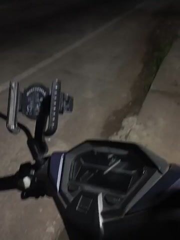 Here is a description of the video:

The video shows a nighttime scene from the perspective of someone sitting on a scooter. The scooter's dashboard and handlebars are visible in the foreground. The road stretches out into the darkness, illuminated by streetlights.  A truck passes by on the road. The overall environment appears quiet and dimly lit.