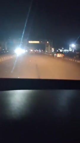 A car is driving at night on a lit road. There are other cars on the road. The road has a barrier on either side. The car is passing under a large sign that reads "EDUCATION, HEALTHCARE, GROWTH." There are some objects that appear to be trash in the road.
