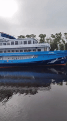 Blue and white cruise ship passes under a stone aqueduct canal