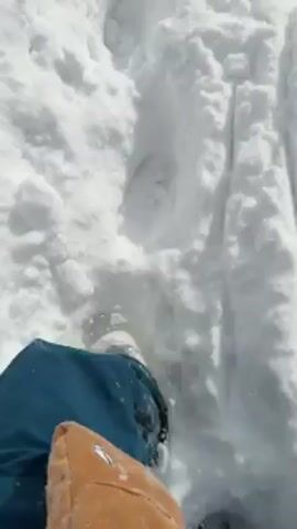 The video begins with a close-up of deep footprints in the snow. The camera pans up to show the path of the footprints leading away into a field covered in deep snow. At the end of the field are bare trees in the distance. The sky is overcast and cloudy.