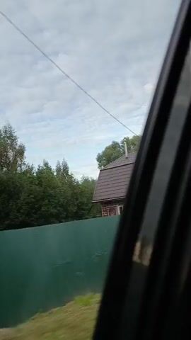 This video captures a forward-facing view from a vehicle moving along a two-lane road. The sky is overcast, with clouds creating a diffused light. On either side of the road, there is abundant vegetation, including trees and tall grasses. The road itself appears to be asphalt, with a white line marking the lane separation. Several cars are visible on the road, traveling in the same direction as the recording vehicle. The scene suggests a rural or semi-rural setting during daylight hours, possibly early morning or late afternoon given the cloud cover and lighting.