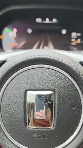 This is a first-person point-of-view video of someone driving a car on a road. The driver's hand is visible on the steering wheel at the beginning of the video. The dashboard display shows various information, including speed and a graphical representation of the road. The car is driving on a paved road that appears to be in the countryside, with trees on either side. There is heavy fog, which significantly reduces visibility. The road is winding and uphill.