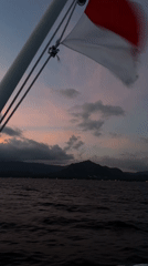 Boat travels Indonesian waters under colorful skies near mountains