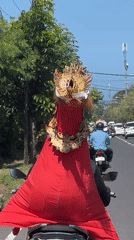 Elaborately costumed rider in mythical mask navigates Denpasar streets