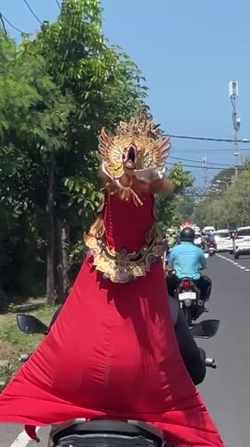 Elaborately costumed rider in mythical mask navigates Denpasar streets