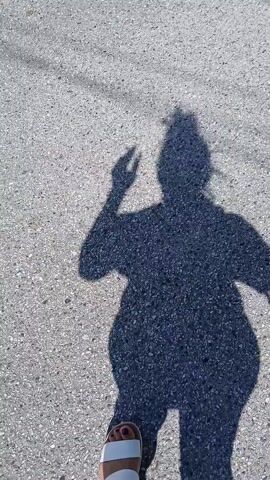 A person's shadow is shown on a gray surface. The person lifts their hand into the air, as though waving. A white shoe with a purple-painted toe then comes into view, as the shadow disappears. The shoe and the gray surface on which it sits, fill the remainder of the video.