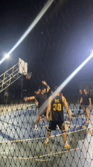 Men play basketball on lit outdoor court in Thailand