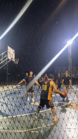 Men play basketball on lit outdoor court in Thailand