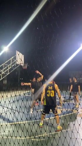 Men play basketball on lit outdoor court in Thailand