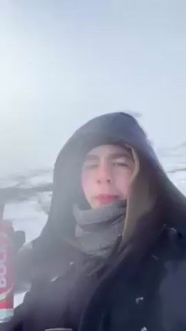 Two young men in winter gear are drinking beer outdoors in a snowy, mountainous environment. One man is holding two cans of “Super Bock Bock” beer. The camera angle is low and slightly tilted upward, suggesting a selfie taken by one of the men. The weather appears cold and foggy.