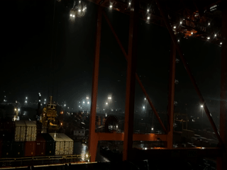 Nighttime shipping port activity observed with orange cranes, wet containers