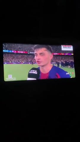 The video shows a person being interviewed after a soccer game. The person is wearing a soccer jersey. The game appears to be between Barcelona and Real Madrid. The interviewee is speaking into a microphone with the logo "LA LIGA EL CLASICO" on it. There is a crowd of people in the background. The score of the game, Barcelona 2 and Real Madrid 0, is visible at the top of the screen. The video seems to be recorded from a television or monitor.