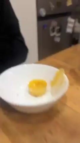A person with curly hair and a black zip-up hoodie, possibly male, is shown close-up, their cheeks puffed out. They open their mouth slightly. The camera then shifts to a white plate with a yellow, gelatinous food item on it, appearing to be partially eaten. The person is then seen again, close-up, with puffed cheeks, looking upwards slightly.