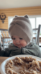 Baby in knitted hat sits for meal in Russian village