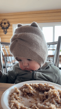 Baby in knitted hat sits for meal in Russian village