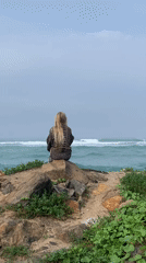 Woman sits oceanside on rocks in Ahangama, Sri Lanka
