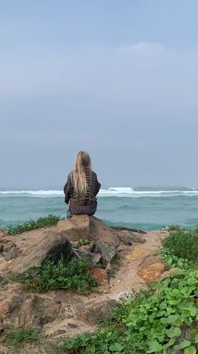 Woman sits oceanside on rocks in Ahangama, Sri Lanka