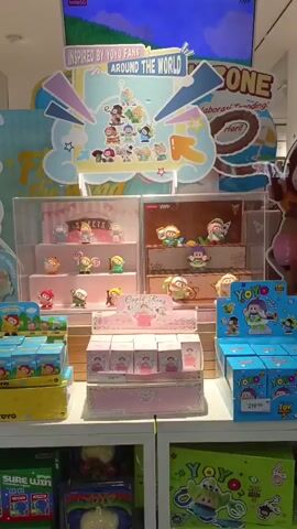 The video shows a display of small collectible toys inside a store. The toys are arranged on tiered shelves within clear plastic cases. A large sign above the display reads "INSPIRED BY YOYO FANS AROUND THE WORLD." The toys appear to be characters from popular animated movies, such as characters from Toy Story. The display is colorful and visually appealing, likely intended to attract customers. The lighting is bright and even, suggesting an indoor retail environment. There are no people visible in the immediate vicinity of the display. The overall impression is one of a toy store or a section of a department store dedicated to collectible merchandise.
