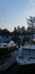 Dusk at the waterfront: boats docked, contrails overhead, tents nearby