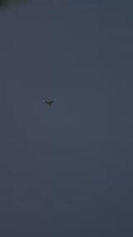 The video shows an airplane flying in the distance against a dark blue sky. The plane has its lights on.