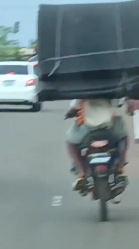 Motorcyclist carries oversized black object through Rido, Nigeria