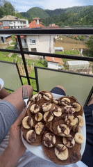 Person enjoys chocolate banana pancakes on balcony breakfast