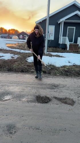 Woman repairs potholes with shovel in rural Russian village