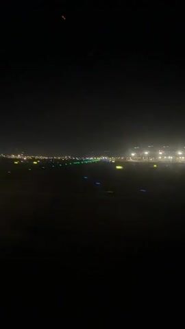 The video shows a view from an airplane window at night. The runway lights are visible, indicating the plane is either landing or taking off. The lights are green and orange. The sky is dark, and city lights are visible in the distance. The plane appears to have just landed as the text says "We have landed."
