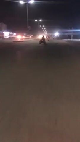 Here's a description of the video:

The video shows a person riding a motorcycle at night. The first shot is from a distance, showing the motorcycle moving away from the viewer on a street with streetlights. The motorcycle appears dark. Then the video switches to a view from the motorcycle itself, focusing on the speedometer. The speedometer reads close to 0 km/h, which might indicate that the motorcycle is idling or moving very slowly. The lighting is low, making details difficult to discern. The street seems empty except for the motorcycle.