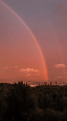 Double rainbow spans a peachy sky over city and forest